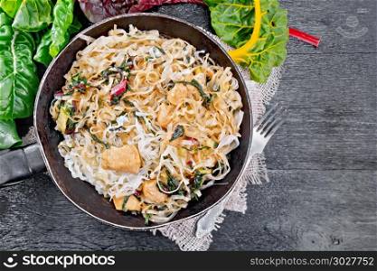 Funchoza with chard and meat in pan on board top. Rice noodles with leafy beet, chicken breast meat, cashew nuts and soy sauce in a frying pan on burlap on wooden plank background on top