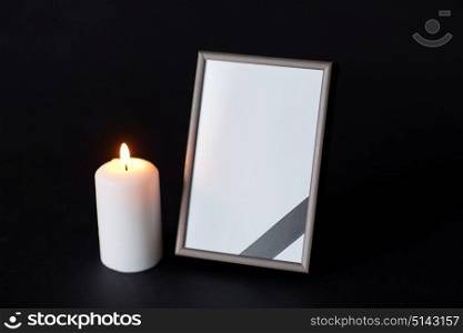 funeral and mourning concept - empty photo frame with ribbon and burning candle over black background. black ribbon on photo frame and candle at funeral