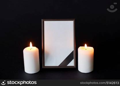 funeral and mourning concept - empty photo frame with ribbon and burning candles over black background. black ribbon on photo frame and candles at funeral