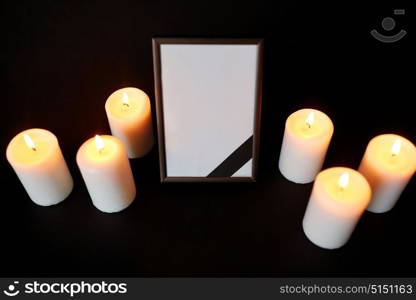 funeral and mourning concept - photo frame with black ribbon and burning candles over dark background. photo frame with black mourning ribbon and candles