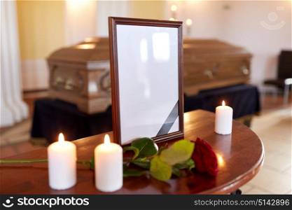 funeral and mourning concept - photo frame with black ribbon, burning candles and coffin at church. photo frame and coffin at funeral in church