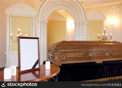 funeral and mourning concept - photo frame with black ribbon, candles and coffin at church. photo frame and coffin at funeral in church