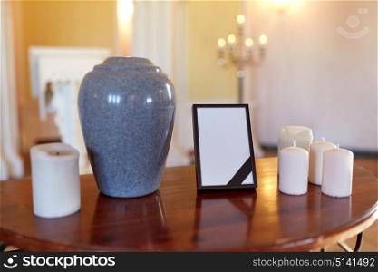 funeral and mourning concept - photo frame with black ribbon, cremation urn and candles on table in church. photo frame, cremation urn and candles in church