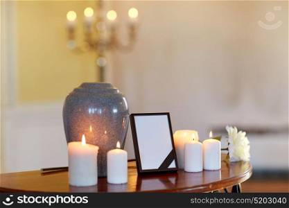 funeral and mourning concept - photo frame with black ribbon, cremation urn and burning candles on table in church. photo frame, cremation urn and candles in church