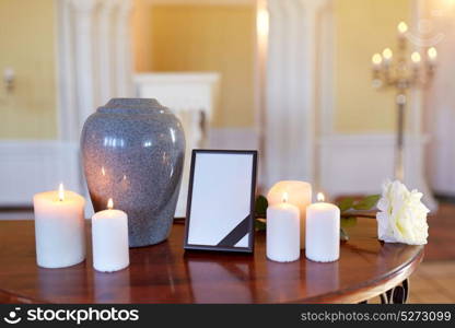 funeral and mourning concept - photo frame with black ribbon, cremation urn and burning candles on table in church. photo frame, cremation urn and candles in church