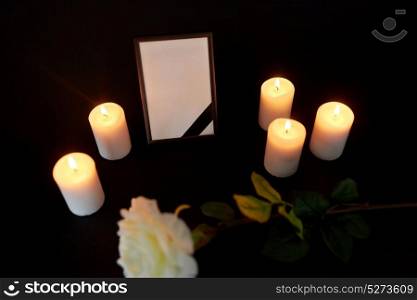 funeral and mourning concept - photo frame with black ribbon, flower and burning candles in darkness. photo frame with black ribbon, flower and candles