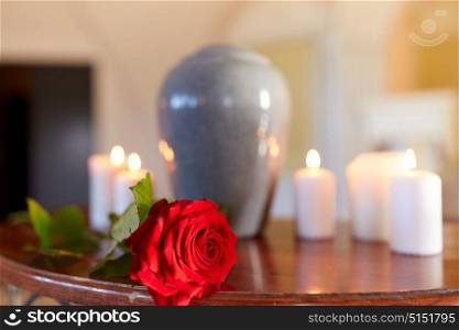funeral and mourning concept - red rose and cremation urn with burning candles on table in church. red rose and cremation urn with burning candles