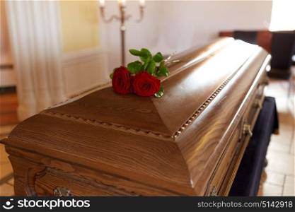funeral and mourning concept - red rose flowers on wooden coffin in church. red rose flowers on wooden coffin in church