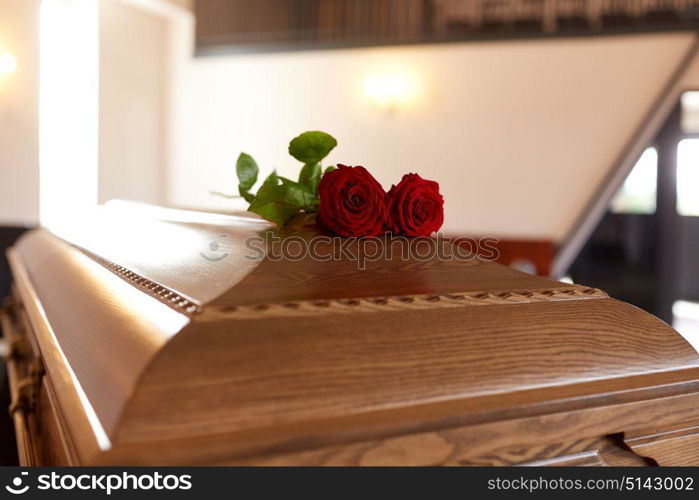 funeral and mourning concept - red rose flowers on wooden coffin in church. red rose flowers on wooden coffin in church