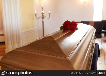 funeral and mourning concept - red rose flowers on wooden coffin in church. red rose flowers on wooden coffin in church
