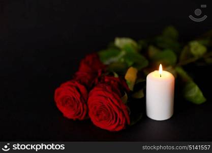 funeral and mourning concept - red roses and burning candle over black background. red roses and burning candle over black background