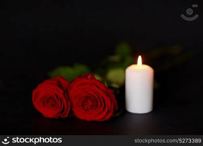 funeral and mourning concept - red roses and burning candle over black background. red roses and burning candle over black background