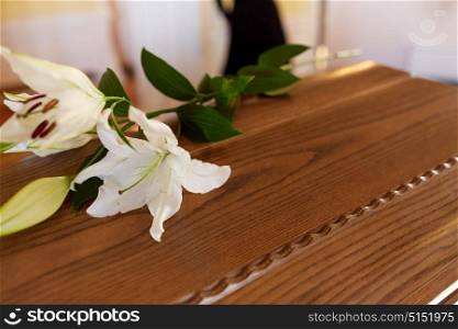 funeral and mourning concept - white lily flower on wooden coffin lid at funeral in church. lily flower on wooden coffin at funeral in church