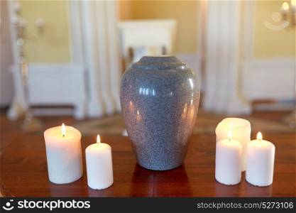 funeral, cremation and mourning concept - funerary urn and candles on table burning in church. cremation urn and candles burning in church