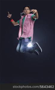 Funky teenage boy jumping in air showing rock and roll sign against black background