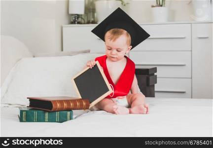 Funny 10 months old baby boy in black graduation cap holding book