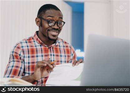 Funny african american man wearing glasses working at laptop grimaces, makes big eyes, realizing missing deadline. Black guy office worker makes faces understanding forgot business meeting.. Funny african american man office worker wearing glasses grimaces, makes big eyes sitting at laptop