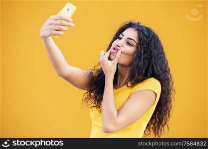 Funny Arab woman taking selfie photograph with smartphone. Curly hair female.. Young Arab woman taking selfie photograph with smartphone.