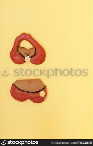 Funny bikini shape gingerbread cake cookie sweet dessert with red icing and yellow flower decoration border or frame on yellow paper background