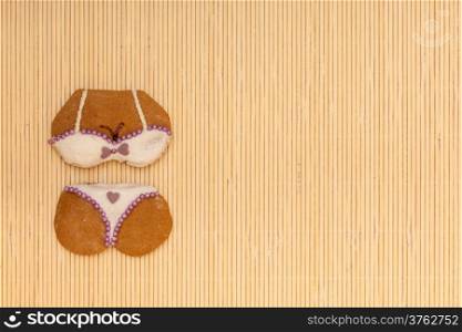 Funny bikini shape gingerbread cake cookie sweet dessert with white icing and violet purple decoration border or frame on beige bamboo mat background