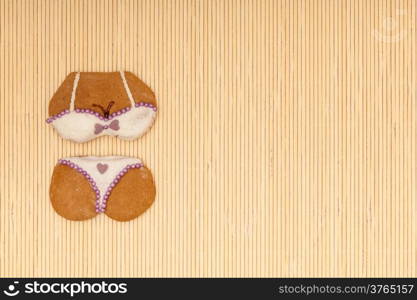 Funny bikini shape gingerbread cake cookie sweet dessert with white icing and violet purple decoration border or frame on beige bamboo mat background