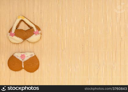 Funny bikini underwear shape gingerbread cake cookie sweet dessert with yellow icing and pink decoration border or frame on beige bamboo mat background