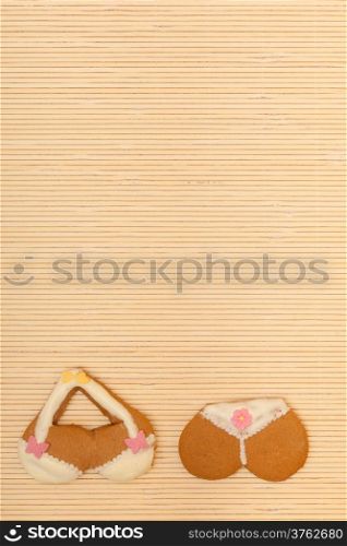 Funny bikini underwear shape gingerbread cake cookie sweet dessert with yellow icing and pink decoration border or frame on beige bamboo mat background