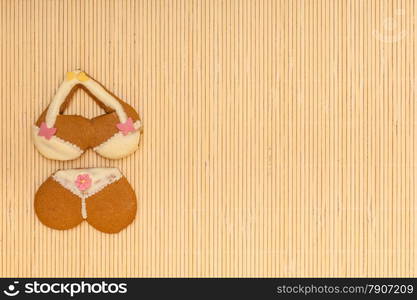 Funny bikini underwear shape gingerbread cake cookie sweet dessert with yellow icing and pink decoration border or frame on beige bamboo mat