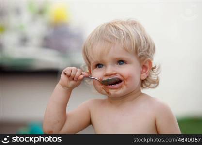 Funny blond baby eating chocolate with a spoon
