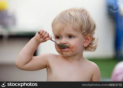 Funny blond baby eating chocolate with a spoon