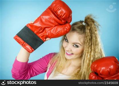 Funny blonde girl female boxer in big fun red gloves playing sports boxing studio shot on blue. Funny girl in red gloves playing sports boxing
