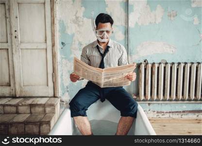 Funny businessman in swimming mask sitting on the edge of the bathtub and reads newspaper. Business fortune concept