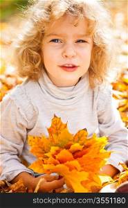 Funny child holding yellow maple leaves in autumn park