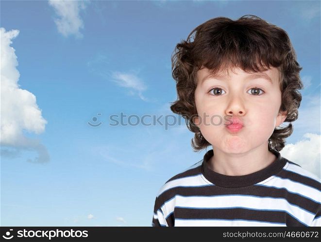 Funny child making grimace throwing a kiss with a blue sky background