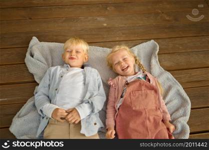 Funny children lying on wooden terrace floor in trailer, summer camping. Family with kids travel in rv car. Campsite adventure, travelling lifestyle, motorhome vacation. Funny children lying on terrace floor in trailer