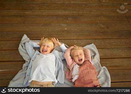 Funny children lying on wooden terrace floor in trailer, summer camping. Family with kids travel in rv car. Campsite adventure, travelling lifestyle, vacation in motorhome. Funny children lying on terrace floor in trailer
