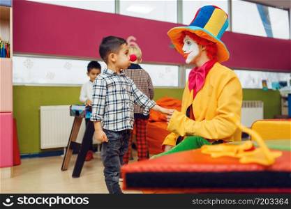 Funny clown and little boy with red nose are playing together. Birthday party in playroom, baby holiday in playground. Childhood happiness, childish leisure. Funny clown and little boy with red nose