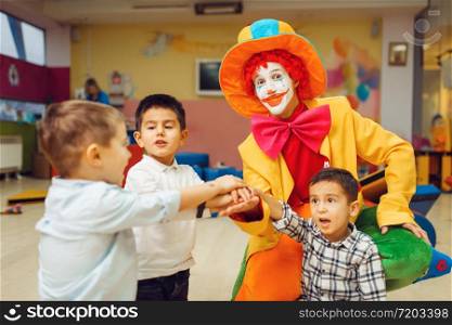 Funny clown and little boys play counting game together. Birthday party celebrating in playroom, baby holiday in playground. Childhood happiness, childish leisure. Funny clown and little boys play counting game