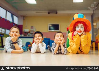 Funny clown and little children lying on the floor. Birthday party celebrating, baby holiday in playground. Childhood happiness, childish leisure. Funny clown and little children lying on the floor