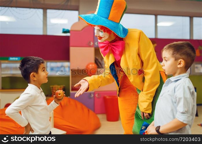 Funny clown animator dancing with little boys in kindergarten. Birthday celebrating in playroom, baby holiday in playground. Childhood happiness, childish leisure. Funny clown animator dancing with little boys