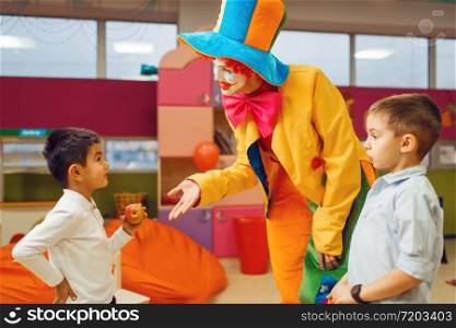 Funny clown animator dancing with little boys in kindergarten. Birthday celebrating in playroom, baby holiday in playground. Childhood happiness, childish leisure. Funny clown animator dancing with little boys