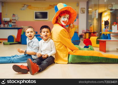 Funny clown animator play with boys in kindergarten. Birthday celebrating in playroom, baby holiday in playground. Childhood happiness, childish leisure, entertainment in children&rsquo;s area. Funny clown play with boys in kindergarten