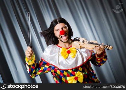 Funny clown plyaing violin against curtain