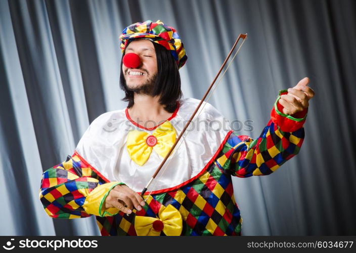 Funny clown plyaing violin against curtain