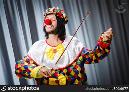 Funny clown plyaing violin against curtain