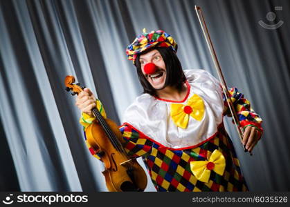 Funny clown plyaing violin against curtain