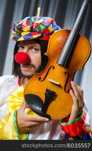 Funny clown plyaing violin against curtain