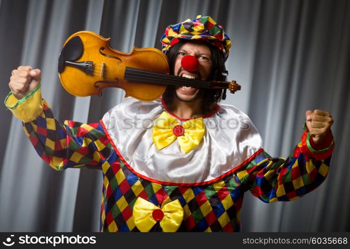 Funny clown plyaing violin against curtain