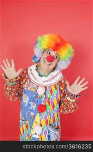 Funny clown with arms raised looking away against colored background