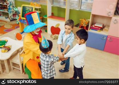 Funny clown with cheerful children play counting game together. Birthday party celebrating in playroom, baby holiday in playground. Childhood happiness, childish leisure. Clown with cheerful children play counting game